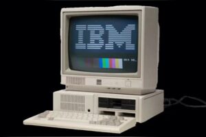 IBM personal computer with a CRT monitor displaying the IBM logo, a keyboard, and a dual floppy disk drive, representing fourth-generation microprocessor-based computing